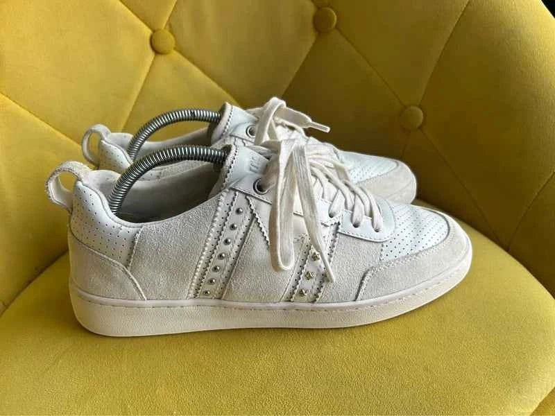 Białe skórzane sneakersy Maje ze srebrnymi nitami na żółtym fotelu, dostępne w sklepie AVEXI