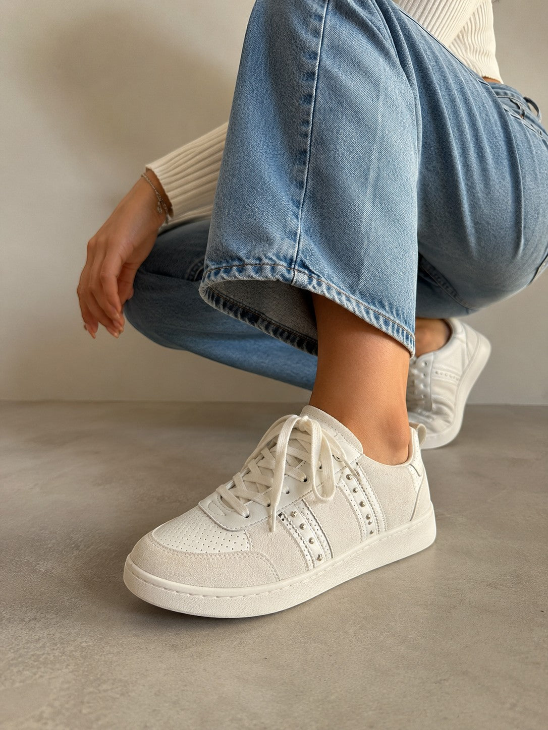 Białe skórzane sneakersy Maje ze srebrnymi nitami na nogach modelki w jeansach, oferta sklepu AVEXI