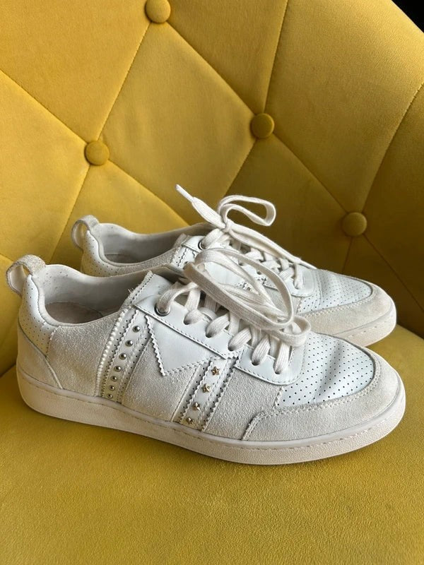 Białe skórzane sneakersy Maje ze srebrnymi nitami i perforacją, dostępne w sklepie AVEXI na żółtym tle.