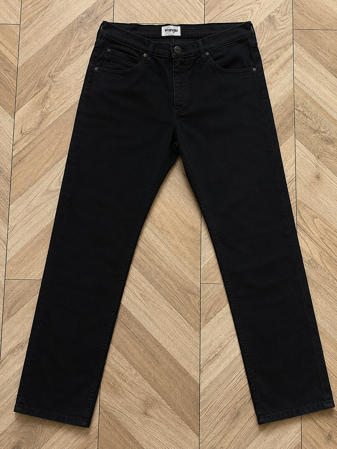 Czarne męskie jeansy Wrangler Arizona z oferty AVEXI, klasyczny krój z pięcioma kieszeniami na drewnianym podłożu.